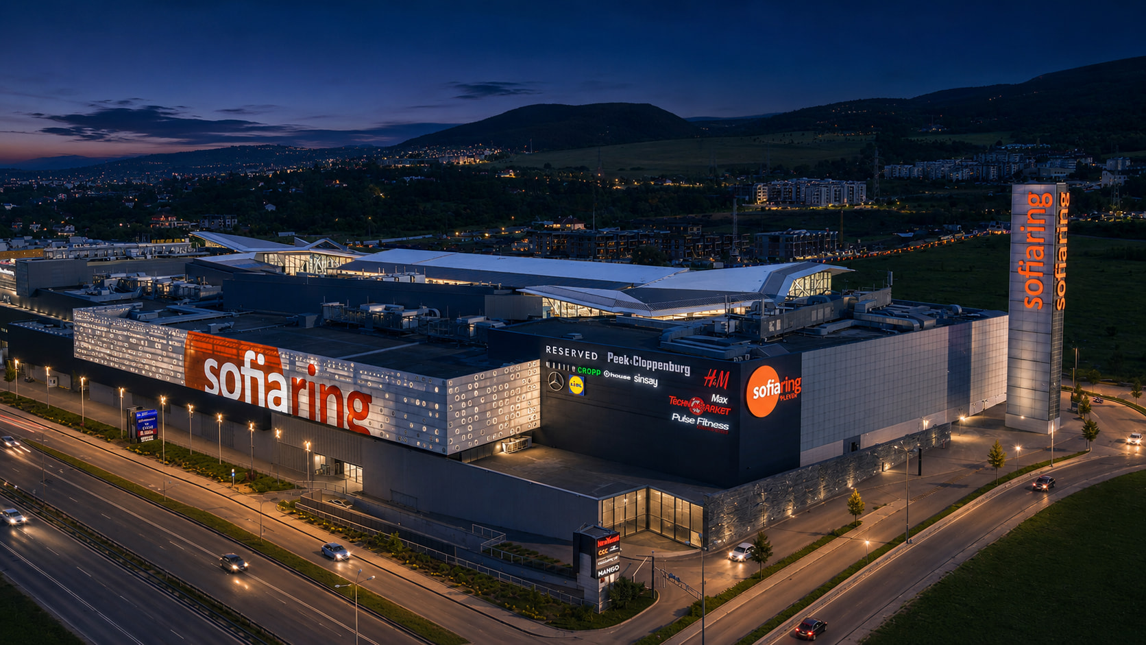 Sofia Ring Mall от птичи поглед привечер — светещите букви на фасадата и планината зад мола